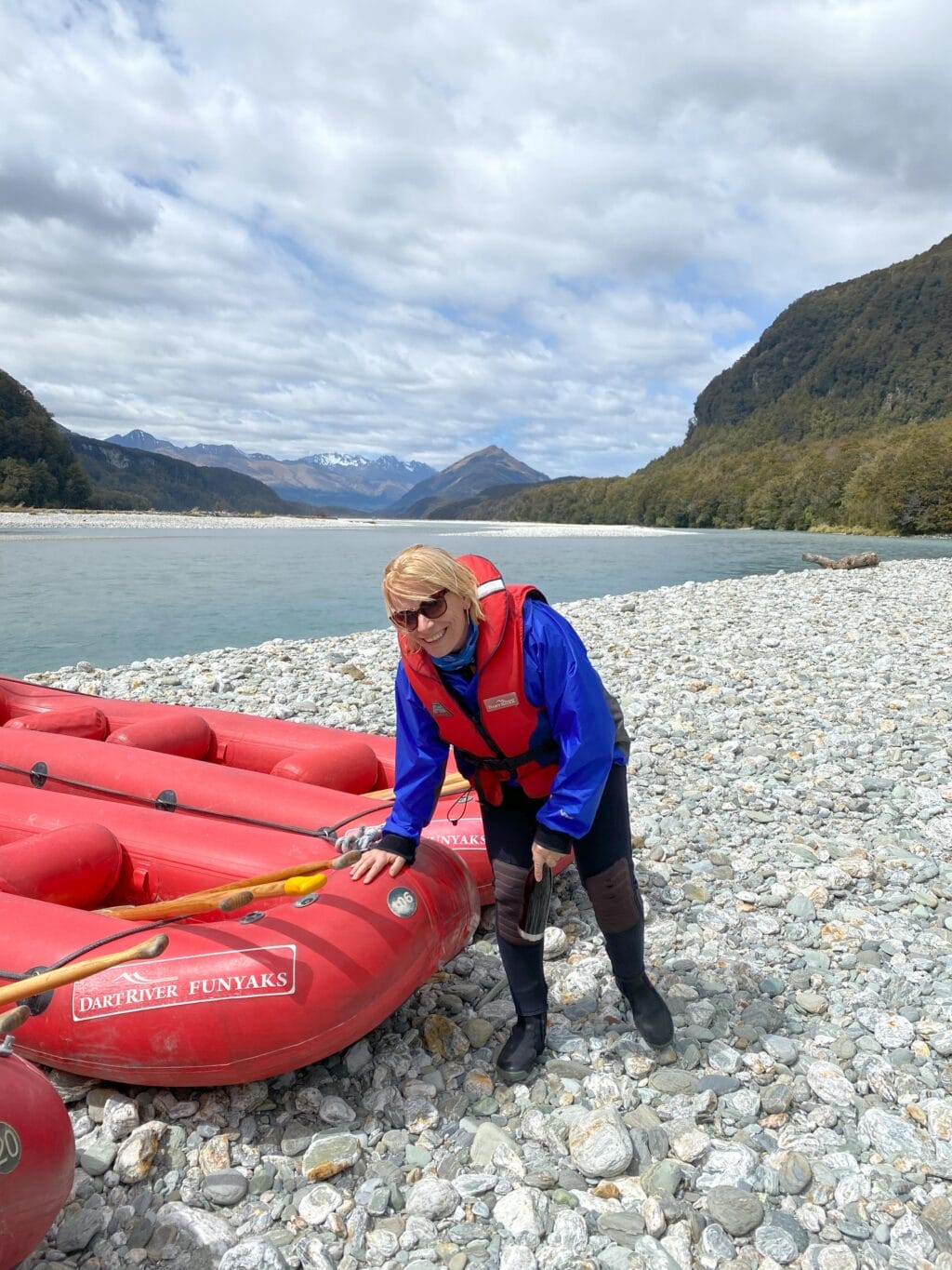 Rotes Schlauchboot für Dart River Funyaks am Kiesufer in Neuseeland mit Bergen und Fluss im Hintergrund.