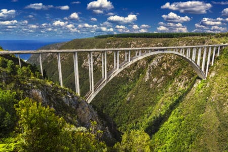 Bloukrans Bridge in Südafrika über einer grünen Schlucht mit Meer im Hintergrund, beliebter Spot für Bungee-Jumping.